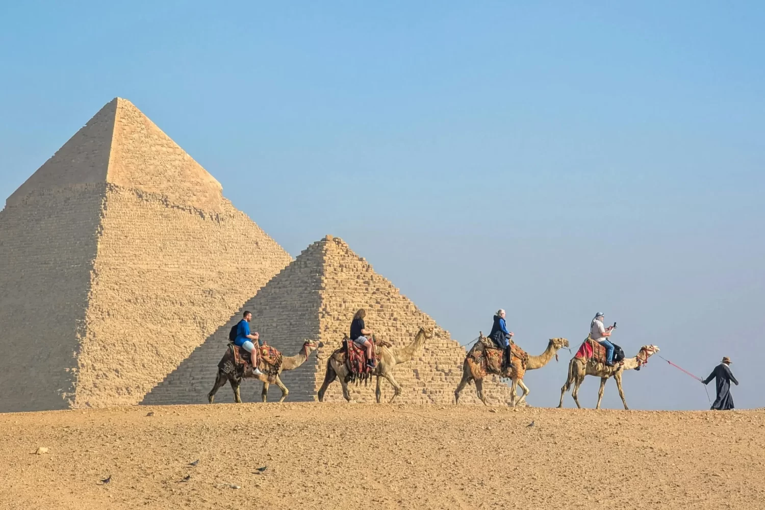 Paseo en Camello en Las Pirámides de Guiza Turistas montando camellos frente a las majestuosas Pirámides de Giza disfrutando del desierto egipcio