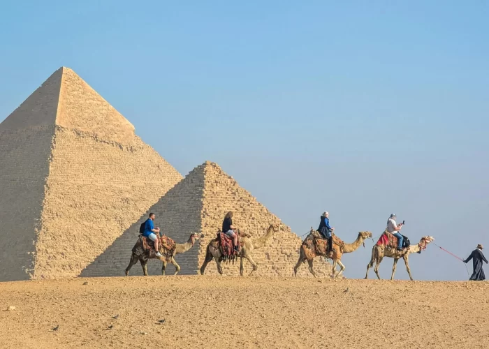 Paseo en Camello en Las Pirámides de Guiza Turistas montando camellos frente a las majestuosas Pirámides de Giza disfrutando del desierto egipcio