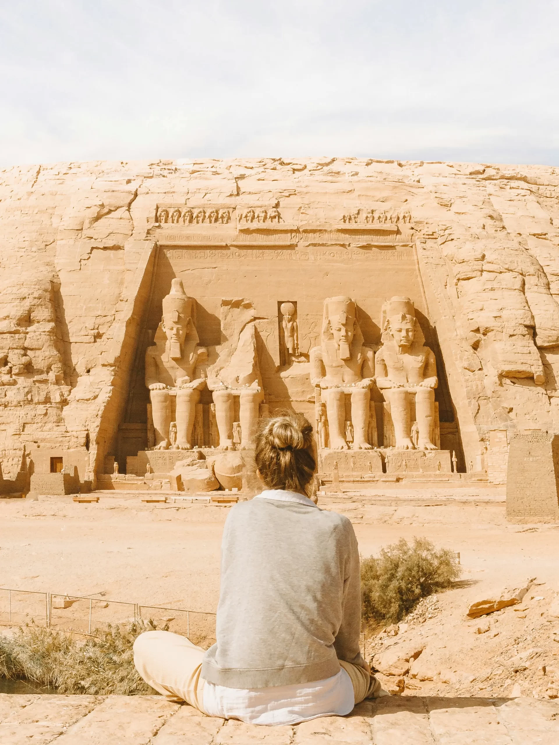 Visitante admirando la fachada de El Templo de Abu Simbel y las estatuas colosales de Ramsés II en Egipto.
